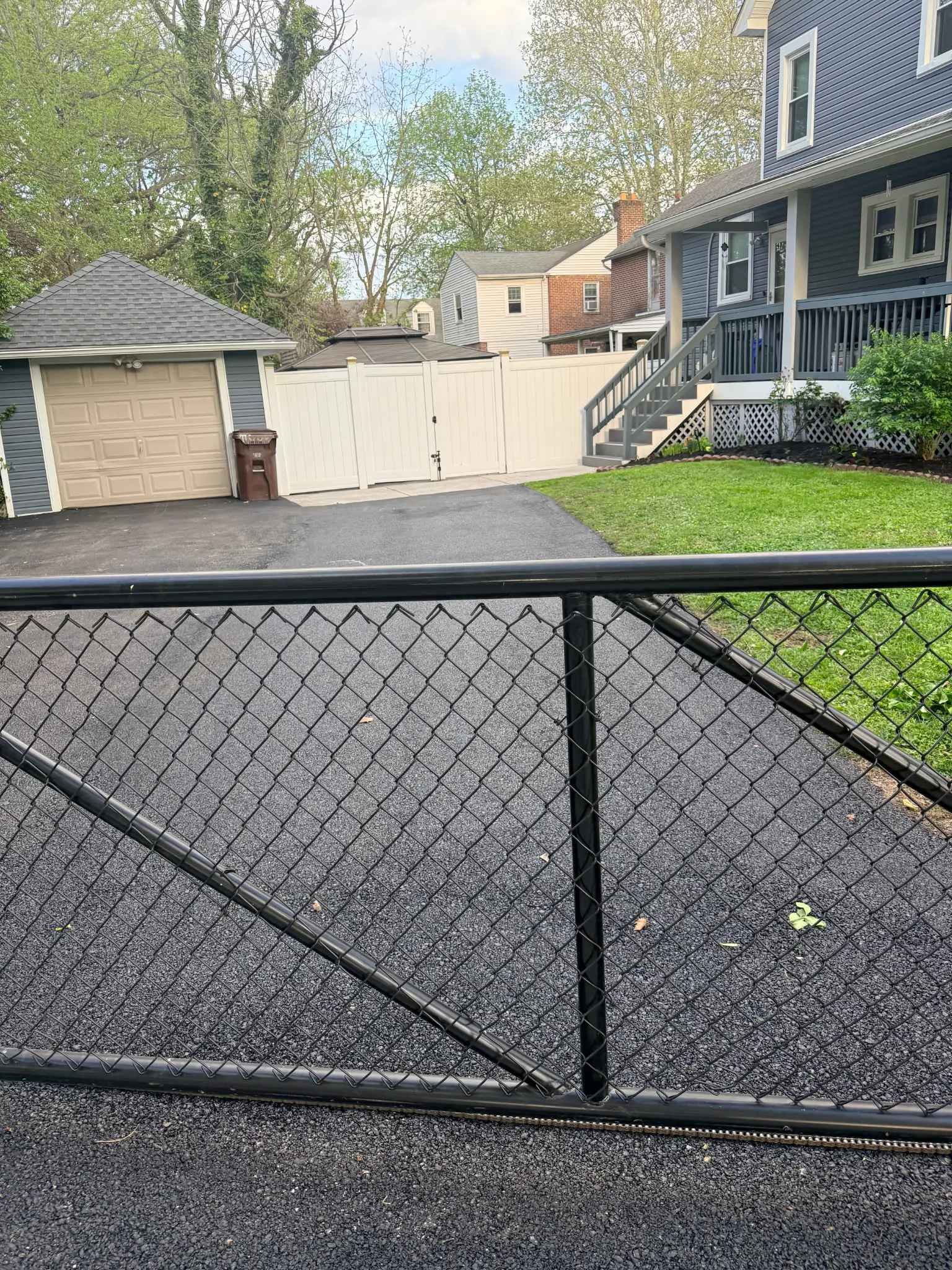 View through a chain-link gate of a freshly paved residential driveway in Chester County