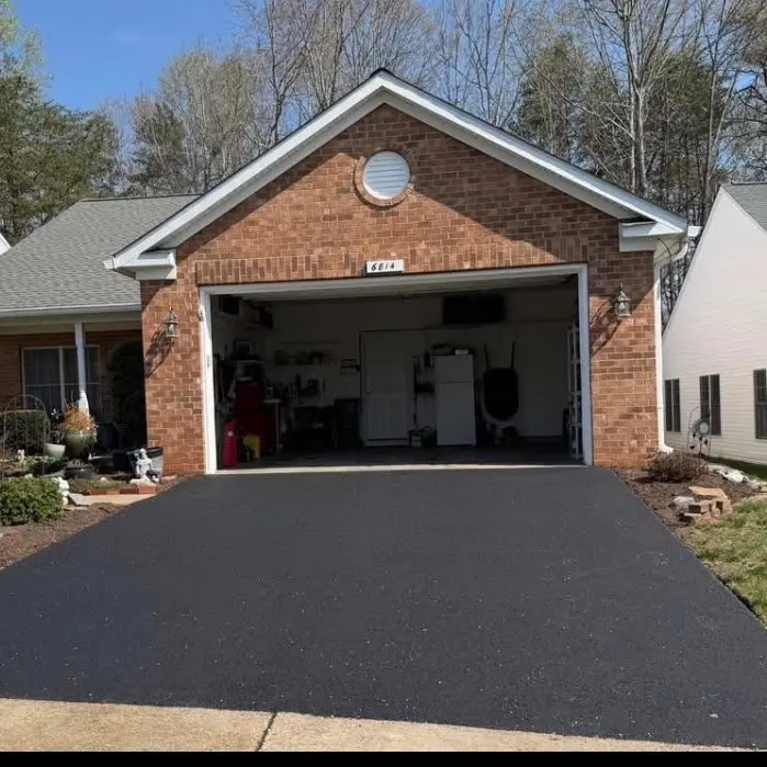 Fresh black asphalt driveway leading to an open garage at a brick residential home